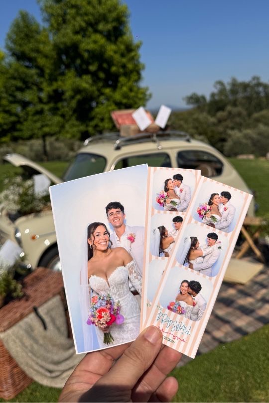 Manos sosteniendo la foto y las tiras del fotomatón de Jeanelle y Jose, con un Escarabajo vintage al fondo — boda en Can Ribas de Montbui