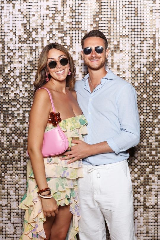 Pareja de invitados posando con gafas de sol frente al fondo dorado del fotomatón — Villa Golf, Sitges